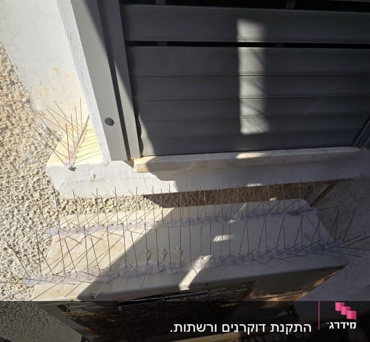 דוקרנים על מזגן ליד חלון בניין